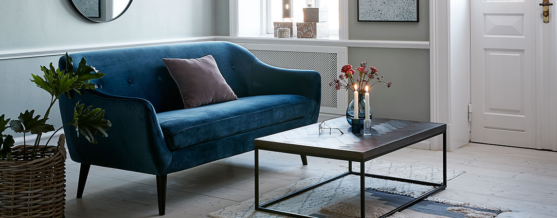 The EGEDAL sofa in blue velvet and HALSKOV coffee table Living room with a blue velvet sofa and a coffee table with lit candles