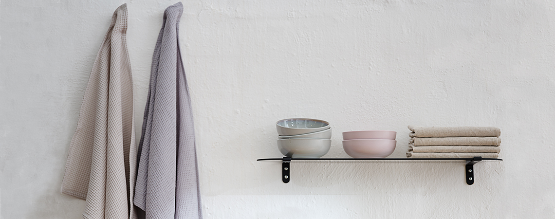 Tea towels hanging next to a glass shelf with bowls and cloth napkins