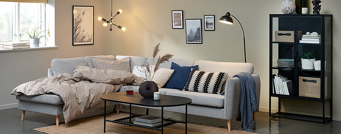 AARHUS open-end sofa, HINNERUP coffee table with decorations and VIRUM display cabinet Living room “hygge” with big corner sofa, duvet, cushions and lighting