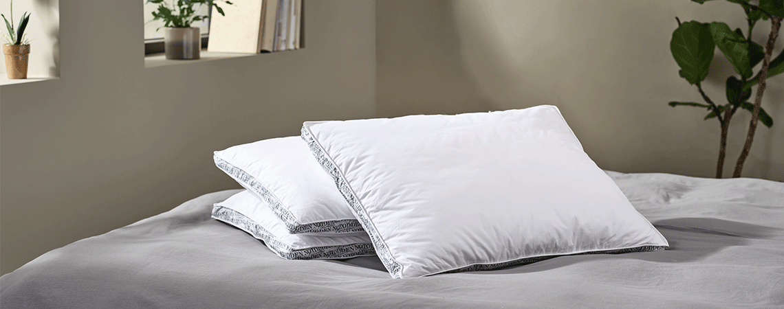 Three different pillows on bed with grey bed linen