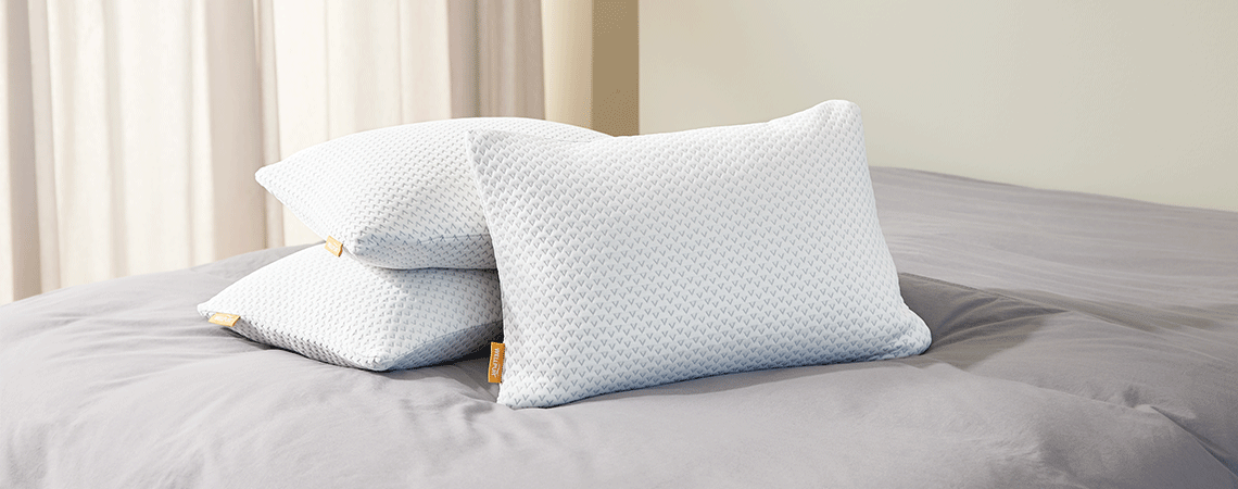 Read our pillow price guide Three different pillows on grey bed linen