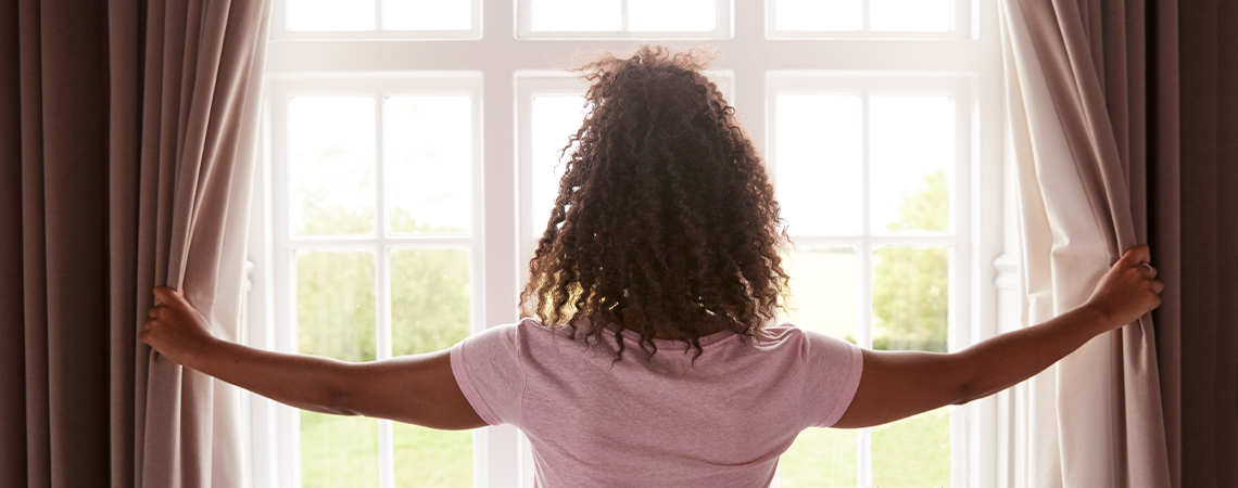 Curtains are not just for pleasing the eye, but also for improving the comfort of your home Woman is drawing heavy curtains in front of bright, white windows