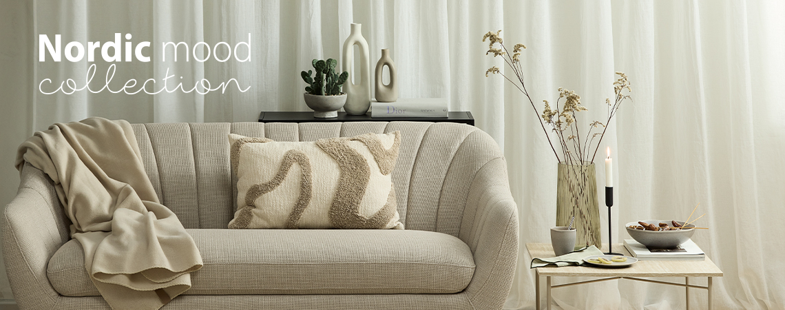 Sofa with throw and tufted cushion in front of white vase and next to end table with vase, candlestick and bowl