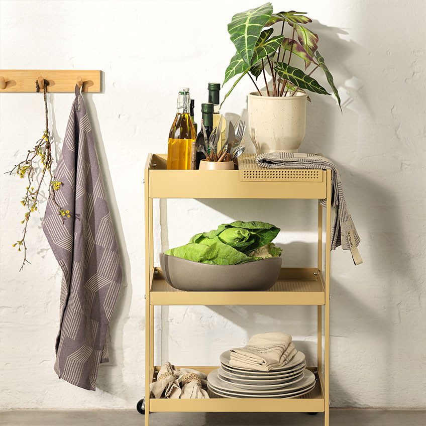 LERK tea towel, VEGARD bowl, and MARIUS artificial plant in ADAM plant pot Tableware on trolley in kitchen with dinner plates, large bowl, cutlery set, and artificial plant