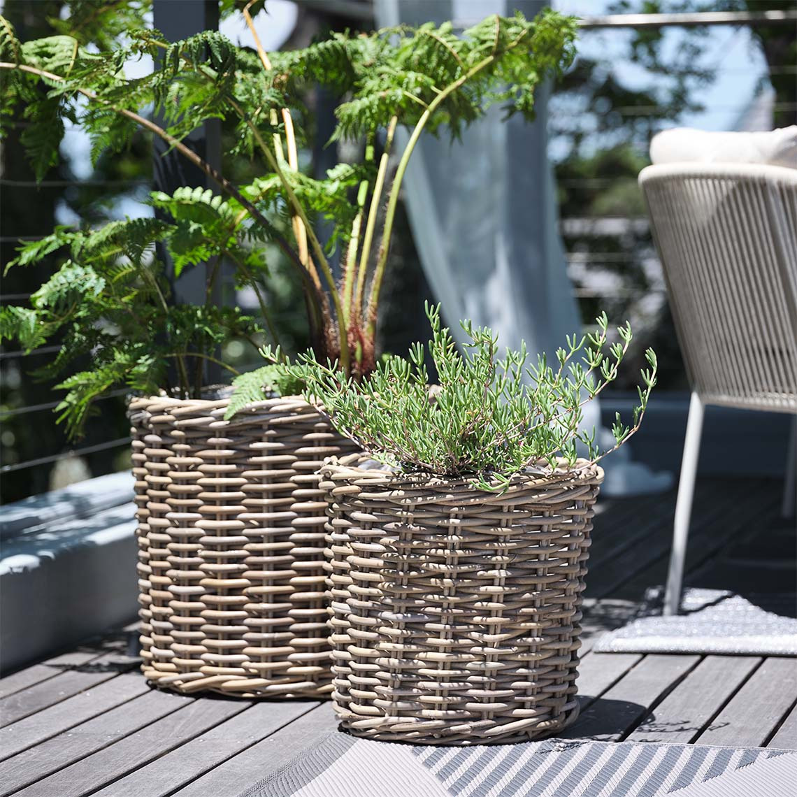 SEGLA garden planter made from woven rattan is available in two sizes Natural rattan garden plant baskets with plants on sunlit patio