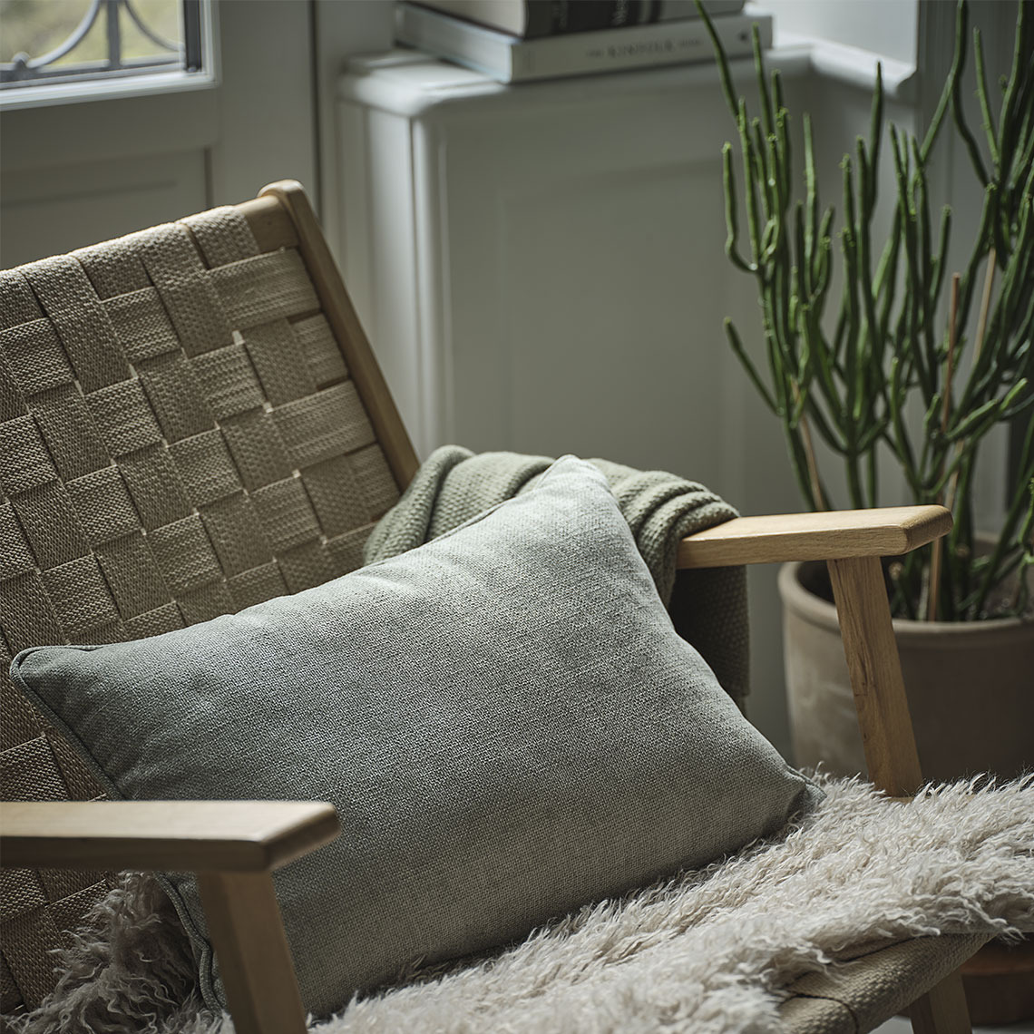 HORNFIOL cushion and KORSKNAP lambskin Green cushion in a chair with a green throw and a beige lambskin