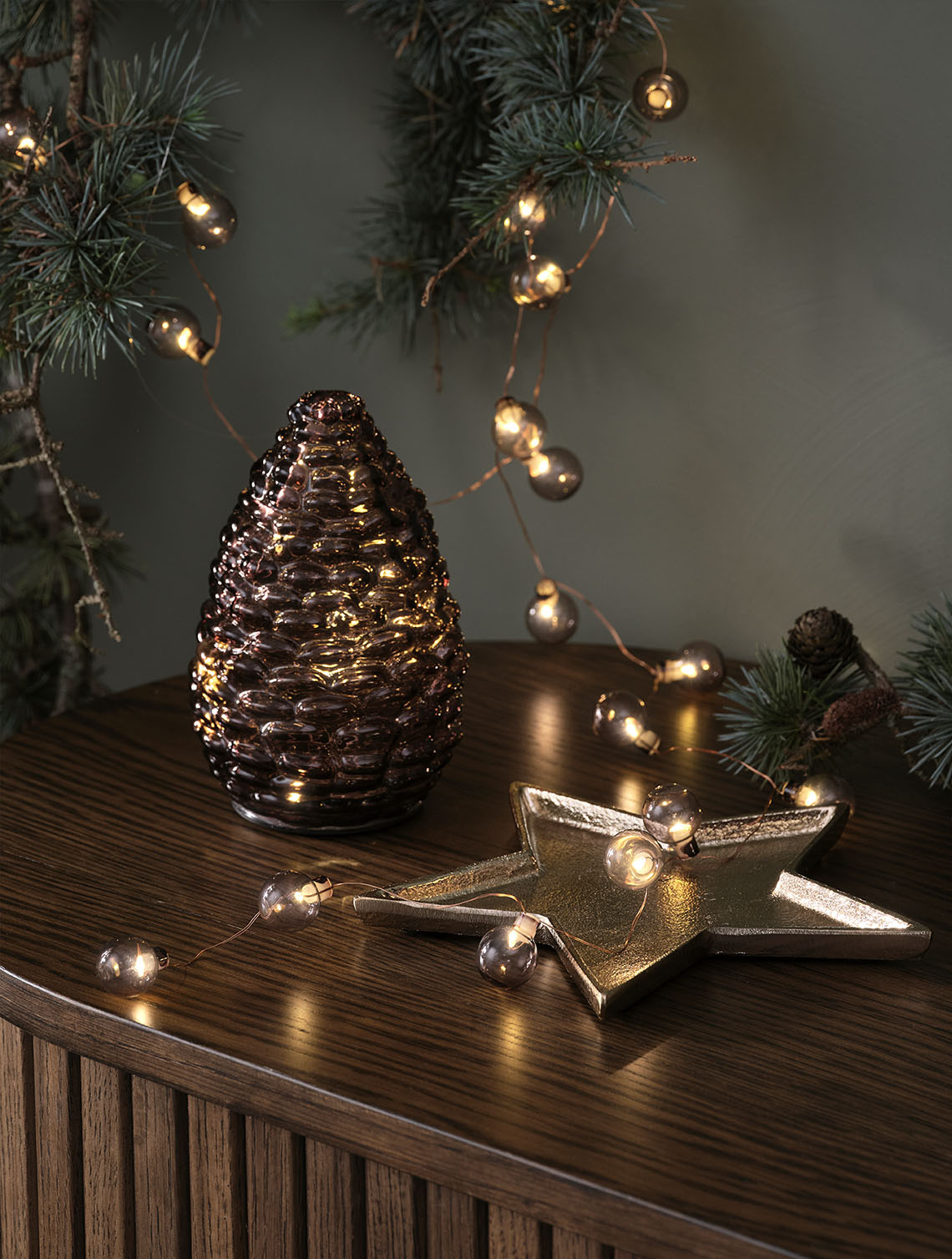 DELLING Christmas cone and ALV string lights Decorative Christmas lighting such as a glass pinecone and golden bauble string light on a sideboard top