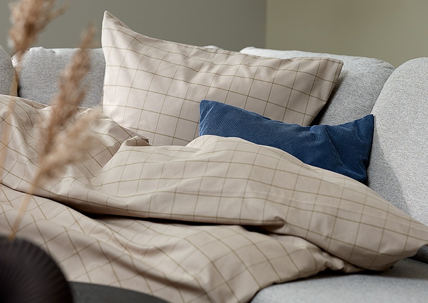 TANJA yarn died duvet cover set in cotton and DUSKULL cushion cover in corduroy Duvet in a yarn died duvet cover set in the corner of a sofa