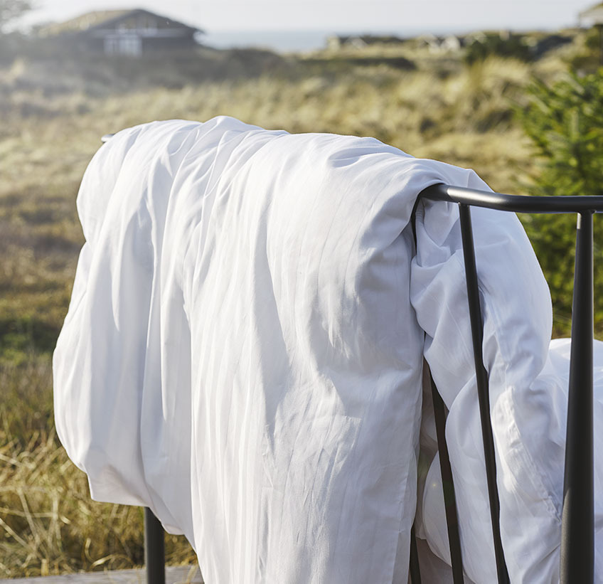 NELL is a long-lasting duvet cover set in a soft sateen weave Duvet hanging over a fence in a natural setting